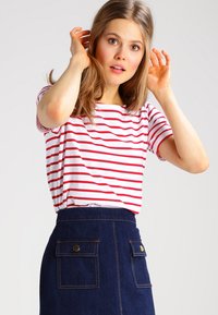 T-shirt a righe rosse e bianche con maniche corte, abbinato a una gonna di jeans scura con tasche frontali e dettagli in metallo dorato.