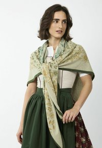 Châle en laine avec des motifs floraux en vert, jaune et bleu. Surdimensionné, drapé autour des épaules, il complète une robe traditionnelle avec une jupe verte.