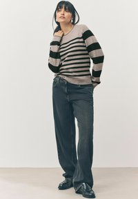 Pull rayé en tissu gris clair et noir, avec des manches longues et un col rond. Associé à un jean sombre ample et des mocassins noirs.