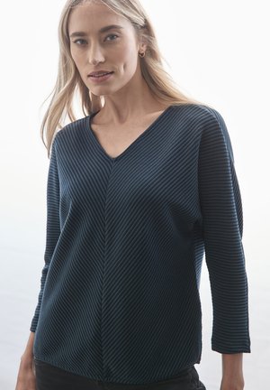 Marinblus med långt ärm och V-ringning samt asymmetriska sömmar. Mjuk textur med horisontella linjer, något avslappnad passform.