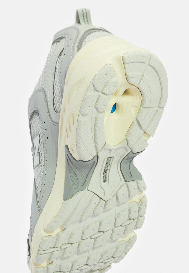 Chaussure de sport gris clair avec tige en maille, semelle intermédiaire avec amorti et semelle extérieure en caoutchouc texturé avec des détails moulés en crème et bleu contrastants.