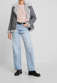 Grå jacka med fårskinnsfoder, ljusrosa kabelstickad tröja, ljusblå högmidjade jeans, svarta snörstövlar och ett svart bälte.