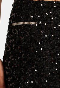 Zwarte paillettenrok met een gestructureerde oppervlakte. Kenmerkt zich door een horizontale kristalaccent nabij de zak voor extra detail.