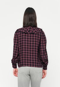 Checkered blouse featuring a ruffled collar, in dark navy with red and white stripes. Long sleeves, relaxed fit, smooth texture.