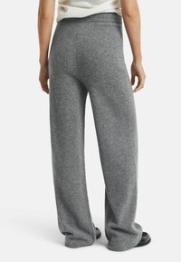Person wearing loose, high-waisted gray knit pants standing with hands relaxed by sides, visible from the back.