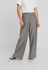 Grijze glitter wijde broek met een elastische tailleband, gecombineerd met een grijs t-shirt en zwarte sneakers. Geweven, vloeiende uitstraling.