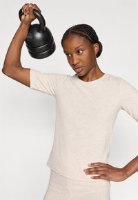 Μαύρο κιτλμπελ που υψώνεται πάνω από το κεφάλι, κρατημένο από ένα άτομο με ανοιχτό μπεζ κοντομάνικο πλεκτό τοπ. Λεπτή επιφάνεια και ουδέτερο χρώμα.