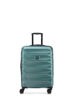 Valigia rigida color teal con quattro ruote rotanti, maniglia telescopica estesa e logo circolare al centro frontale.