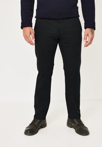 Schwarze Chinos mit Seitentaschen und schmalem Schnitt, kombiniert mit dunklen Schnürschuhen, präsentiert mit einem gestrickten marineblauen Pullover.