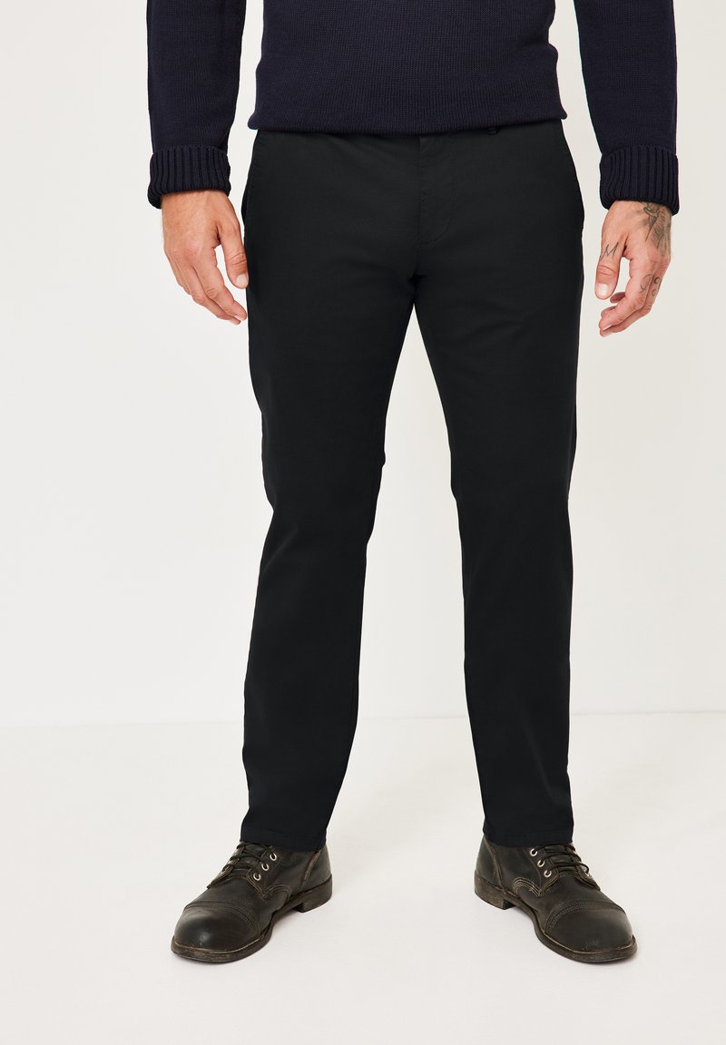 Schwarze Chinos mit Seitentaschen und schmalem Schnitt, kombiniert mit dunklen Schnürschuhen, präsentiert mit einem gestrickten marineblauen Pullover.