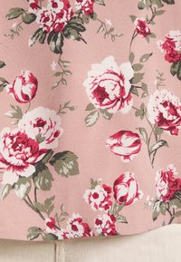 Tecido floral com fundo rosa, apresentando grandes rosas vermelhas e brancas acompanhadas de folhas verdes, exibindo uma textura suave e um bordado intricado.