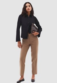 Zwarte button-up blouse, beige tailored broek, zwarte ballerina's, bruine clutch. Glad materiaal, aansluitend ontwerp en subtiele texturen.