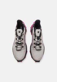 Scarpe da ginnastica grigio chiaro con dettagli rosa, lacci neri e tomaia in rete testurizzata. Presentano una suola imbottita con grip distintivi.
