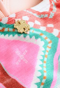 Spalvota audinys su tekstūriniu raštu, kuriame dominuoja rožinės, žalios ir oranžinės spalvų motyvai, papuoštas auksiniu dekoratyviniu spaustu, puoštame gėlių detalėmis.