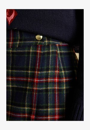 Granatowy dzianinowy sweter nałożony na plisowaną spódnicę w kratę z zielonymi, czerwonymi i żółtymi tonami, zdobioną złotymi guzikami i z teksturowanej wełnianej tkaniny.