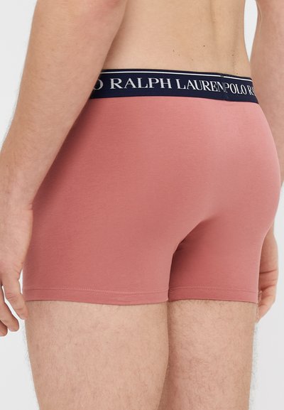 Męskie bokserki w miękkim różowym materiale, z granatową gumą z logo w pasie oraz dopasowanym krojem o gładkiej fakturze bez widocznych wzorów.