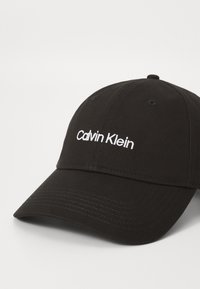 Fekete baseball sapka pamutból, lekerekített koronával, ívelt napellenzővel és fehér hímzett "Calvin Klein" logóval.