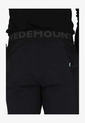 Schwarze Hose mit einem breiten Bund, auf dem "WEDEMOUNT" in Grau steht. Strukturierter Stoff mit einer kleinen, blauen und gelben Akzentuierung an der Seitentasche.