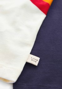 Katoenen T-shirt met een crème kleur op één mouw, een marineblauw lichaam en een klein label waarop "Little Bird" is geborduurd.
