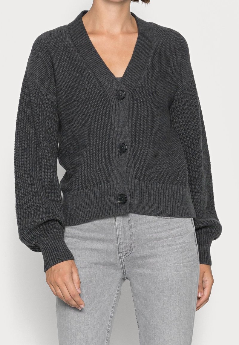 Tmavě šedý pletený kardigan s výstřihem do V, dlouhými rukávy a pěti velkými knoflíky vpředu. Žebrovaná textura s elastickými manžetami a lemem.
