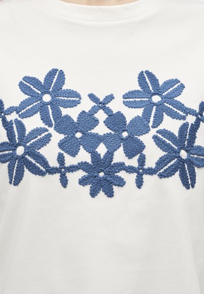 Μπλε κεντητό λουλουδάτο μοτίβο με διάφορα σχήματα λουλουδιών σε λευκό υφασμάτινο φόντο.