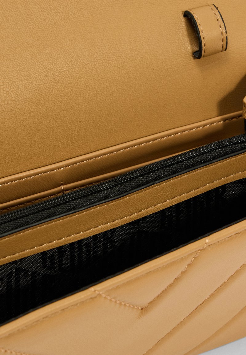 Sac à main en cuir tan avec un motif matelassé, comprenant un compartiment zippé et un intérieur en tissu noir. Texture lisse avec des coutures détaillées.