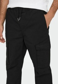 Černé cargo kalhoty s uvolněným střihem, postranními kapsami, nastavovacím páskem se šňůrkou a hladkým, odolným materiálem.