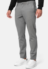 Pantalones gris ajustados hechos de una tela texturizada. Cuentan con un frente plano, bolsillos y se combinan con zapatillas blancas.