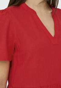 Vestido de lino rojo con escote en V, mangas cortas abullonadas y un diseño de falda en capas. La textura parece ligera y transpirable.