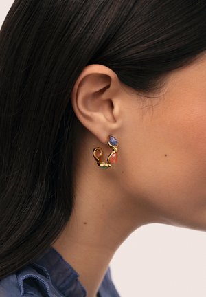 Pendiente de aro dorado con piedras azules, coralinas y verdes, llevado en la oreja izquierda de una persona con cabello oscuro y piel bronceada.