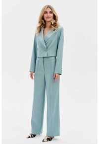 Costume ajusté bleu clair avec une veste à double boutonnage courte et un pantalon à jambes larges, fabriqué à partir d'un tissu lisse. Comprend de grandes boucles d'oreilles.