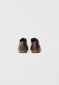 Chaussures en cuir brun à la forme arrondie, avec des coutures décoratives et une finition texturée. Talon en bois avec une semelle lisse et un revêtement en tissu.