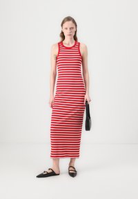 Robe débardeur rayée rouge et blanche, texture côtelée, longueur genou. Associée à des chaussures plates noires et un petit sac à main noir.