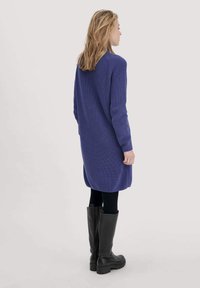 Abito lavorato a maglia viola a maniche lunghe con vestibilità rilassata, caratterizzato da un motivo testurizzato, orlo arrotondato e abbinato a stivali neri fino al ginocchio.