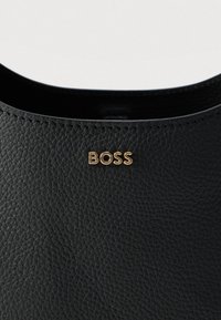 Μαύρη δερμάτινη τσάντα χειρός με υφή στην επιφάνεια και χρυσό λογότυπο "BOSS". Απλός σχεδιασμός με ανοιχτό πάνω μέρος και λείες άκρες.