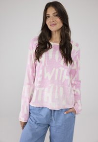 Helles rosa Langarmshirt mit fettem cremefarbenen Text, lockerer Passform und Rundhalsausschnitt. Kombiniert mit hellblauen Zugbandhosen.