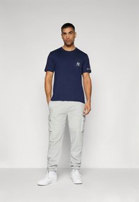 Tmavě modré bavlněné tričko s logem na hrudi, doplněné světlými šedými cargo tepláky s bočními kapsami. Outfit doplňují bílé tenisky.