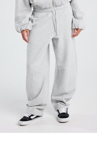 Vaaleanharmaat, painavat collegehousut leveillä lahkeilla, joustavalla vyötärönauhalla ja sivutaskuilla, yhdistetty mustavalkoisiin lenkkareihin.