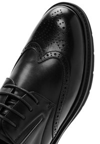 Zwarte leren dresschoenen met brogue-details, een gladde textuur, ronde neus en dunne veters. Beschikt over een duurzame rubberen zool.