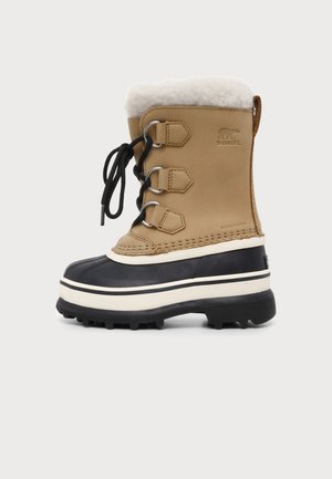 Brun og sort vinterstøvle med tyk sål, hvid pelsforing, snørebånd foran og "Sorel" logo på siden.