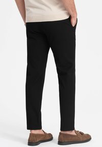 Mustat housut, joissa on kapea istuvuus, sileä pinta ja sivutaskut. Yhdistetty ruskeisiin loafereihin, mikä antaa rentoa ilmettä.