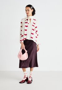 Blouse blanche avec un motif de lèvres rouges, détail en nœud au cou; jupe en satin noir; sac à main rose; chaussettes crème avec des cœurs rouges; chaussures bordeaux.