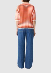Paskowana koszulka w kolorze pomarańczowym i białym z krótkimi rękawami, zestawiona z niebieskimi dżinsami o wysokim stanie i szerokich nogawkach. Prosty tył.