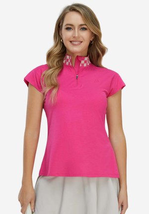 Femme souriante portant un haut à manches courtes rose vif avec une demi-fermeture éclair et un col à carreaux, assorti à une jupe beige clair.