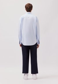 Camicetta azzurra chiara con maniche lunghe, orlo curvo e spacco laterale, abbinata a pantaloni blu navy scuri e sneakers bianche.
