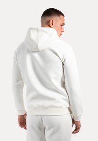 Felpa bianca in cotone con cappuccio strutturato e polsini a costine, caratterizzata da una texture e una vestibilità lisce. La vista posteriore mostra un design minimalista.