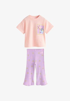 Odjeća za malo dijete s ružičastom majicom kratkih rukava s crtanim psom i cvjetnim aplikacijama, uparena s ljubičastim zvonastim hlačama s malim cvjetnim uzorcima.