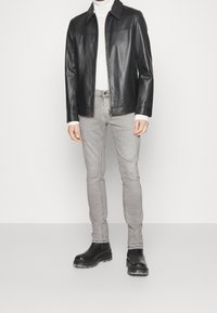 Svart läderjacka med krage, grå åtsittande jeans med slitna detaljer och svarta ankelskor med tjock sula.