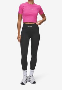 Roze cropped t-shirt met 'PEGADOR' logo, gecombineerd met hoge zwarte leggings met logo band, witte enkelsokken en witte sneakers.