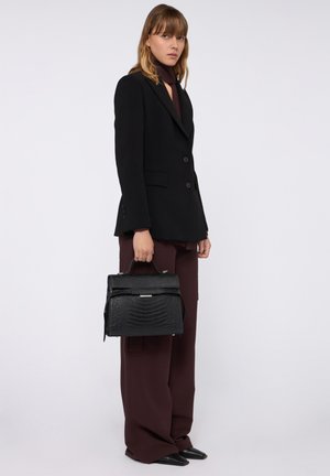 Zwarte gestructureerde handtas met een geprinte krokodillenpatroon, zilveren hardware en een bovenhandvat, gecombineerd met een zwarte blazer en burgundy broek.